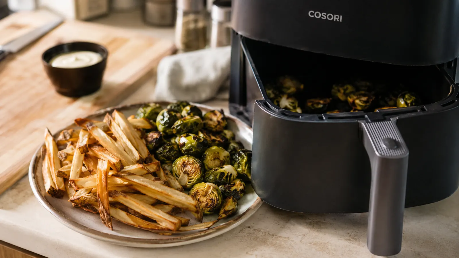 Plate of crisp golden fries and roasted brussels sprouts beside the Cosori Air Fryer Pro's open basket