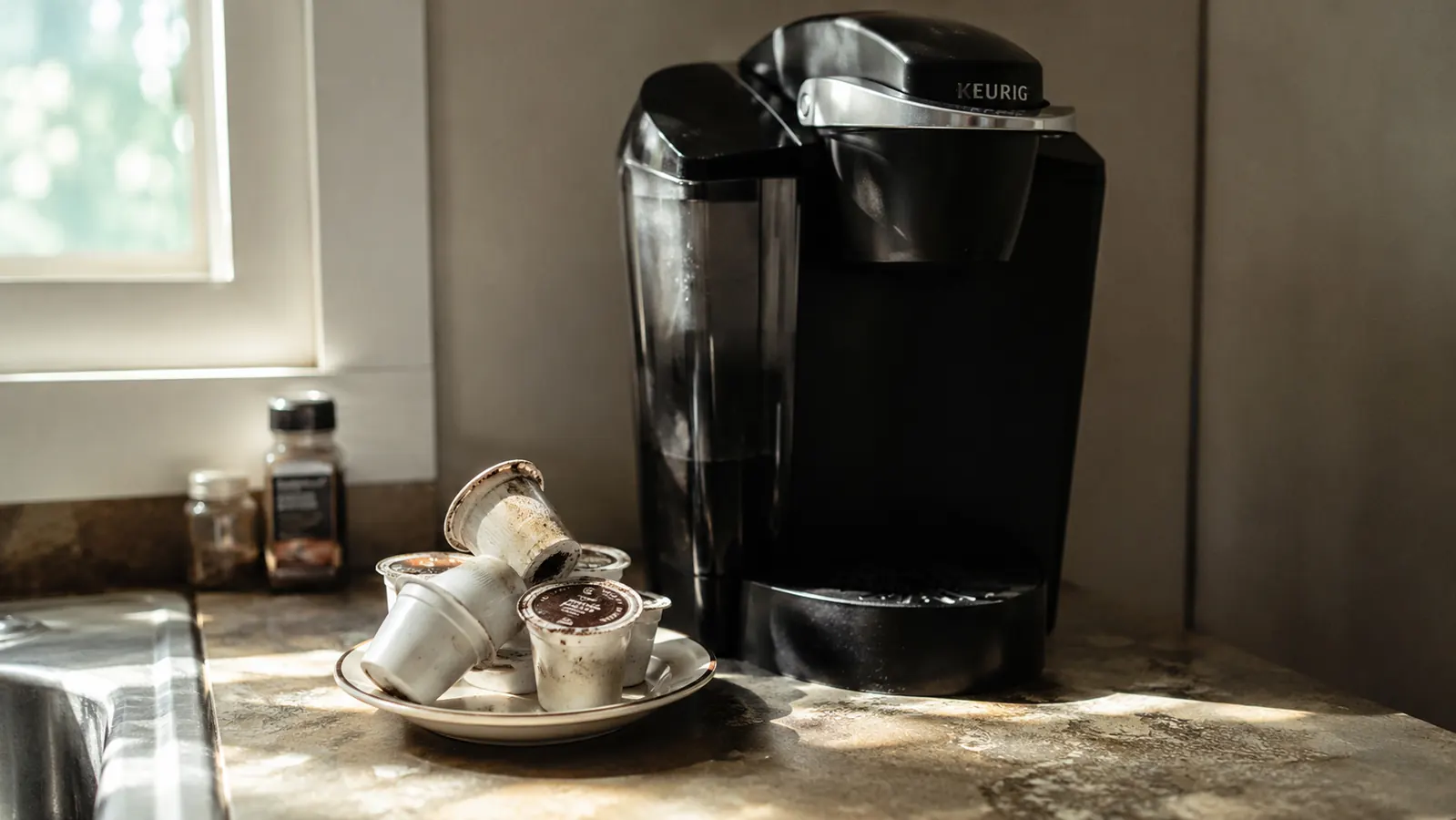A small pile of used coffee pods sitting beside a Keurig K-Classic on a kitchen counter