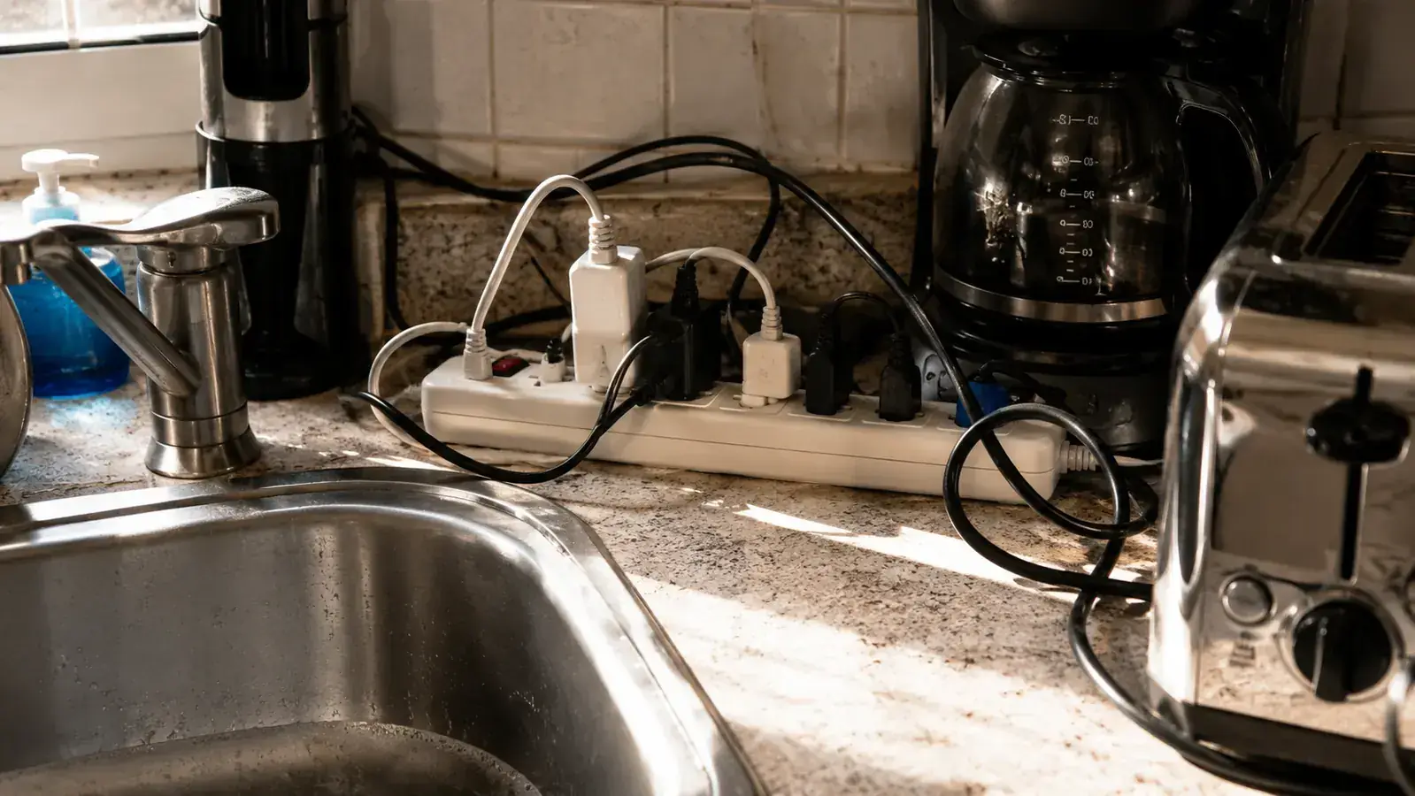 A shared outlet cluster beside a kitchen sink with two appliance cords plugged in